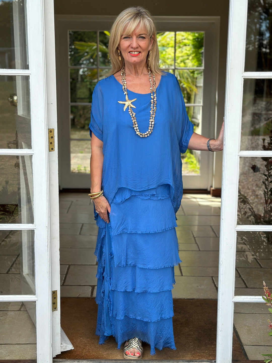 Woman in a blue dress standing in a doorway with a starfish necklace.